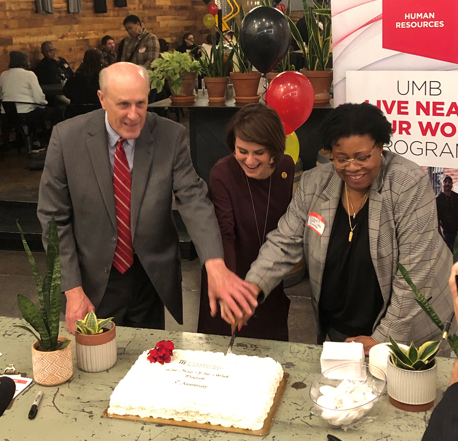 Annie Milli (center), executive director of Live Baltimore, joins UMB President Bruce Jarrell and Dawn Rhodes, senior vice president and chief business and finance officer, to cut the cake.