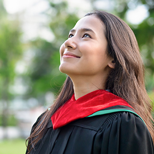 college student dressed in graduation regalia outdoors smiling