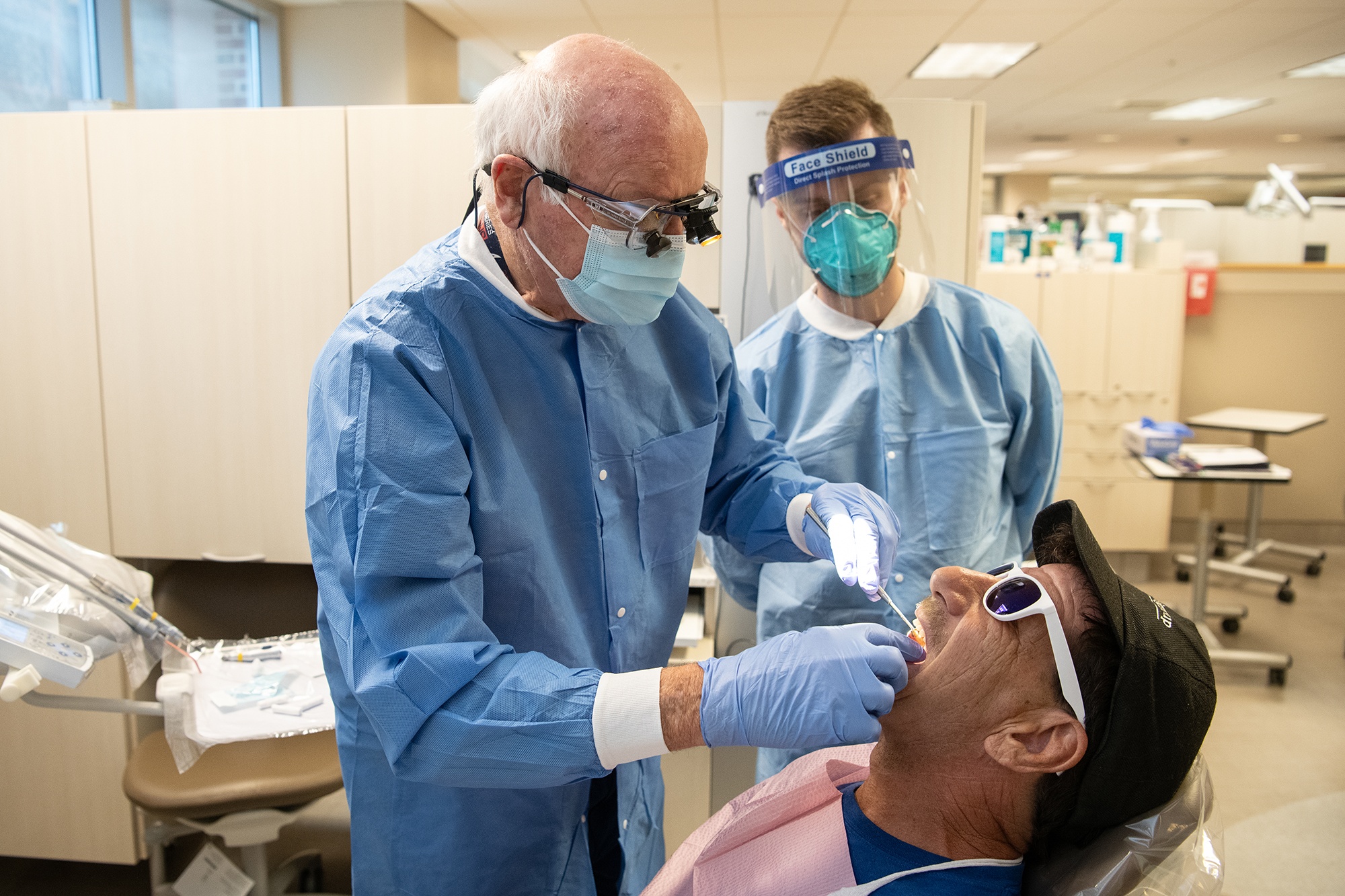 Mark Brennan, DDS, MS, clinical assistant professor at the University of Maryland School of Dentistry, works on patient Scott Phenicie while student Stephen Brockbank observes.  