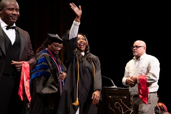 LyAvia Patterson, BSN ’24, waves to the audience as she crosses the stage in front of Yolanda Ogbolu, the dean of the University of Maryland School of Nursing, who is immediately to Patterson’s left.