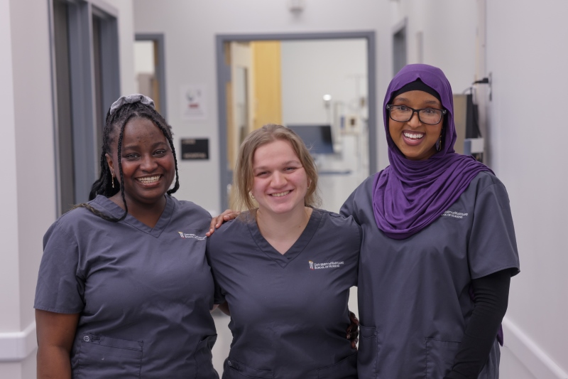 three entry into nursing BSN students wearing gray scrubs and standing in the Hospital Suite at USG