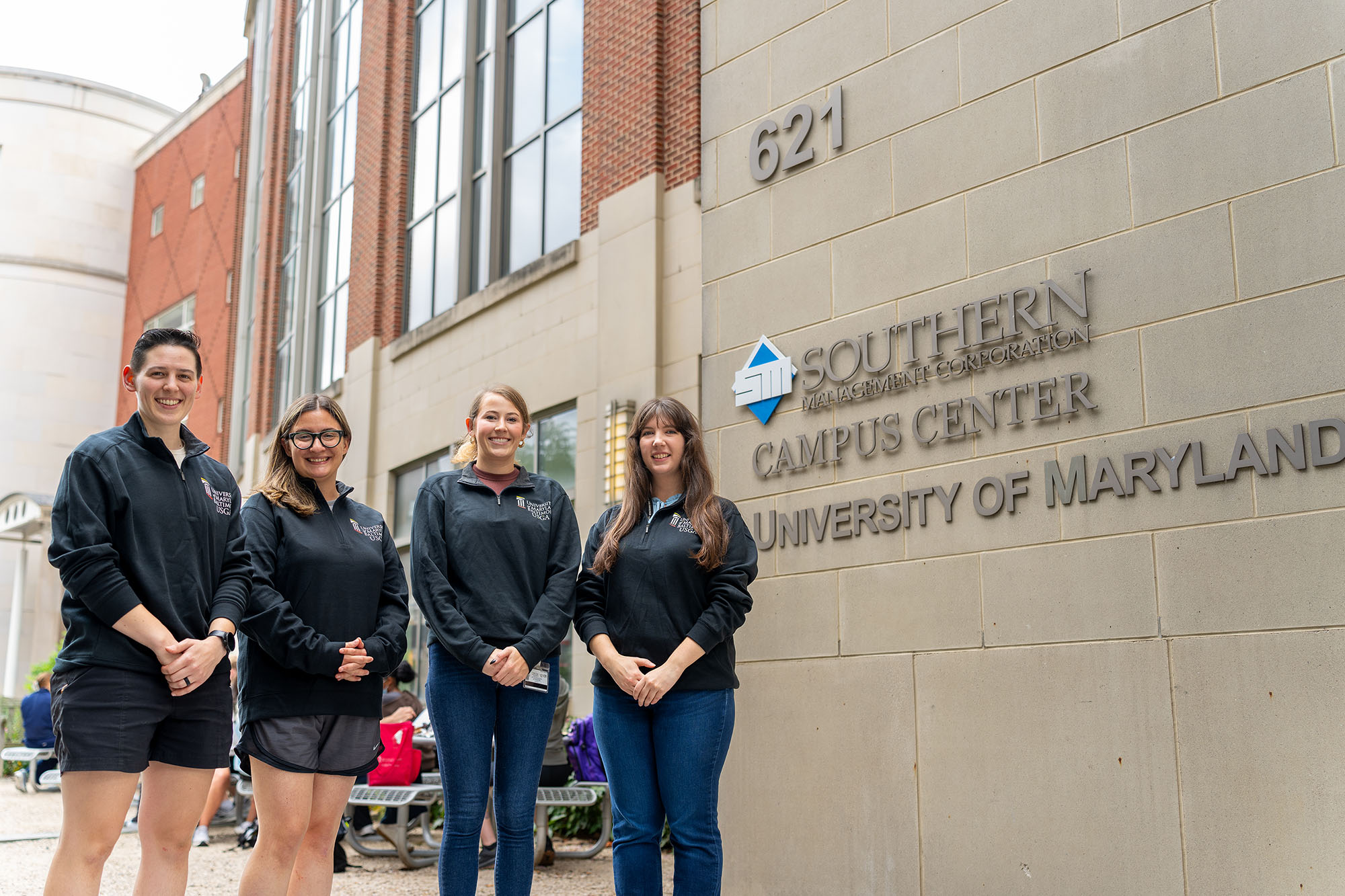 Four students smiling in front of the SMC Campus Center