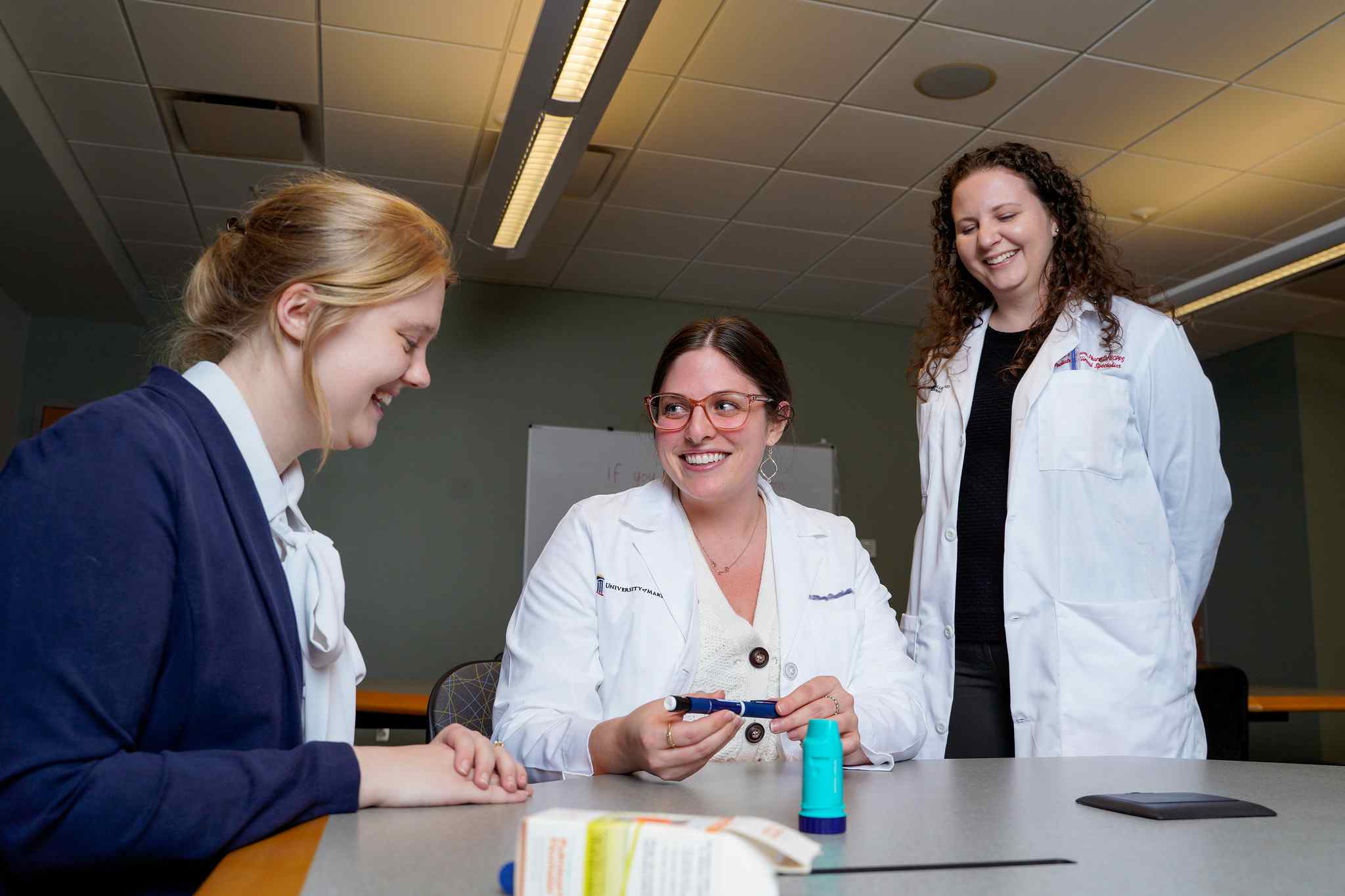 A patient sits at a table learning about medication from a student pharmacist and a preceptor. 