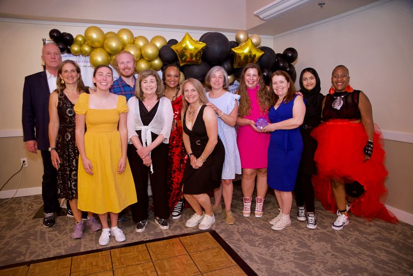 Group posing with award in front of balloon arch