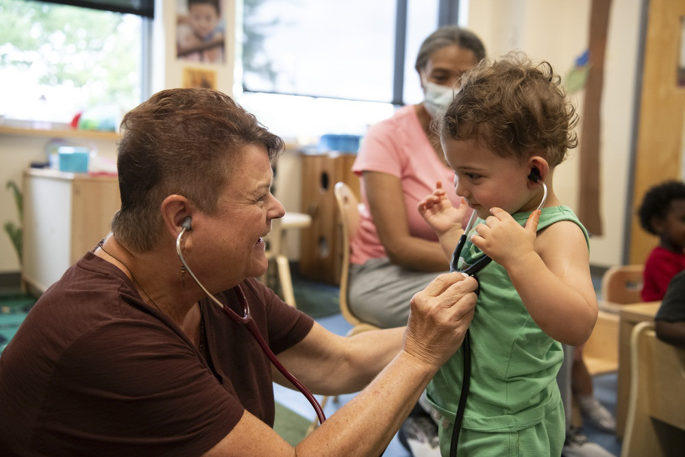 Woman and toddler using stethoscopes in a classroom setting.