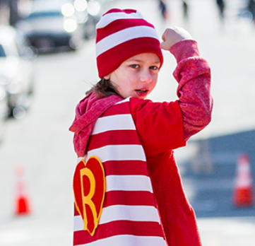 A child wears a Ronald McDonald House cape and flexes their bicep.