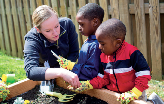 Yates plants seeds with Waverly Early Head Start children in the community garden.