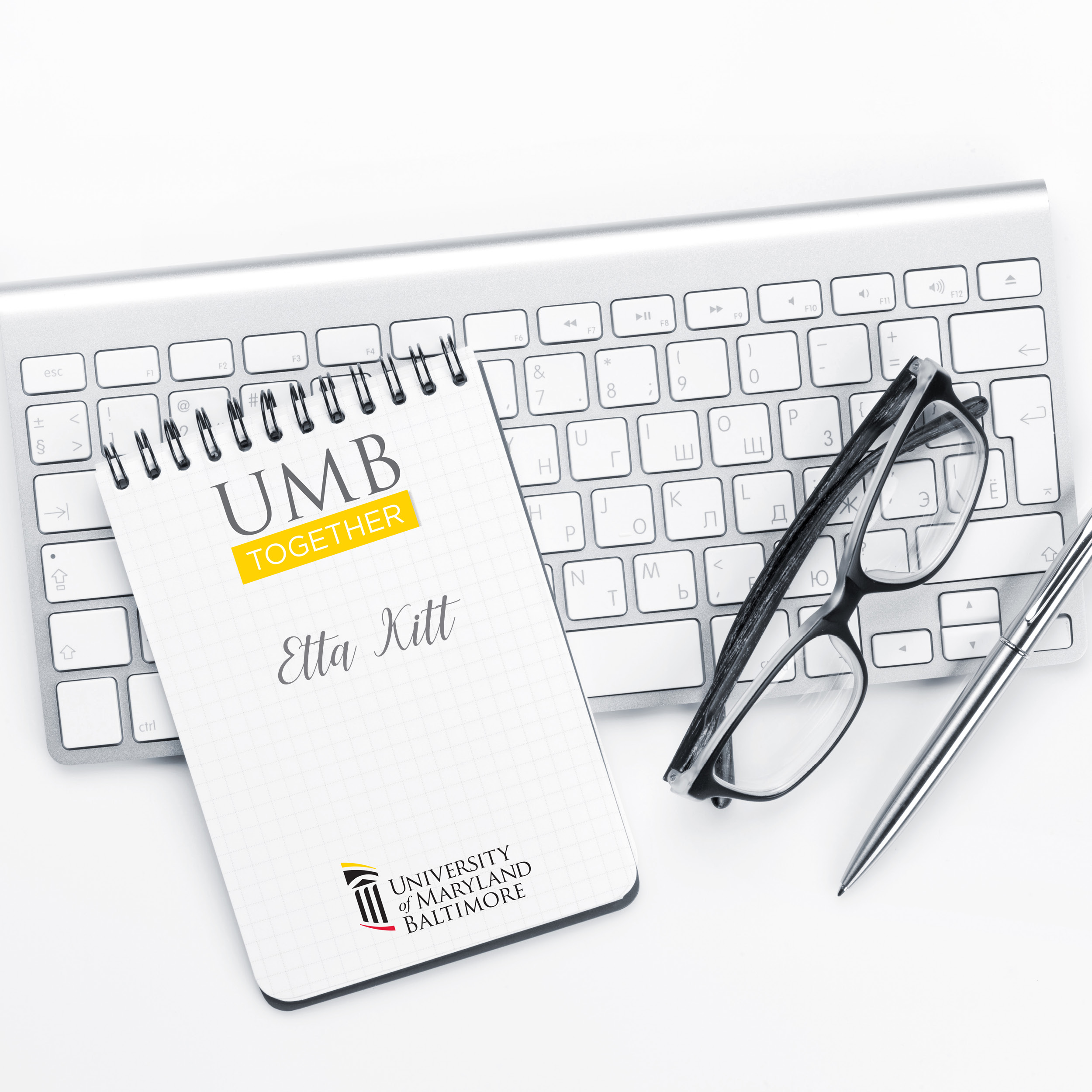 keyboard with UMB Together notebook and eyeglasses on it