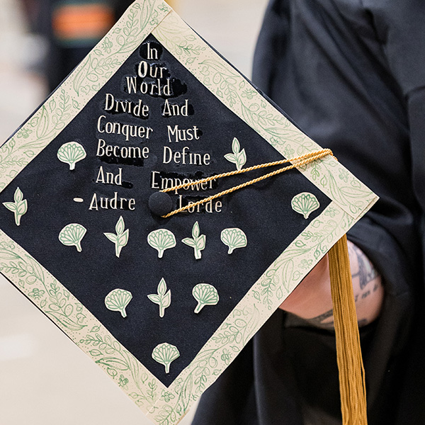 graducation cap that says In our world, divide and conquer must become define and empower