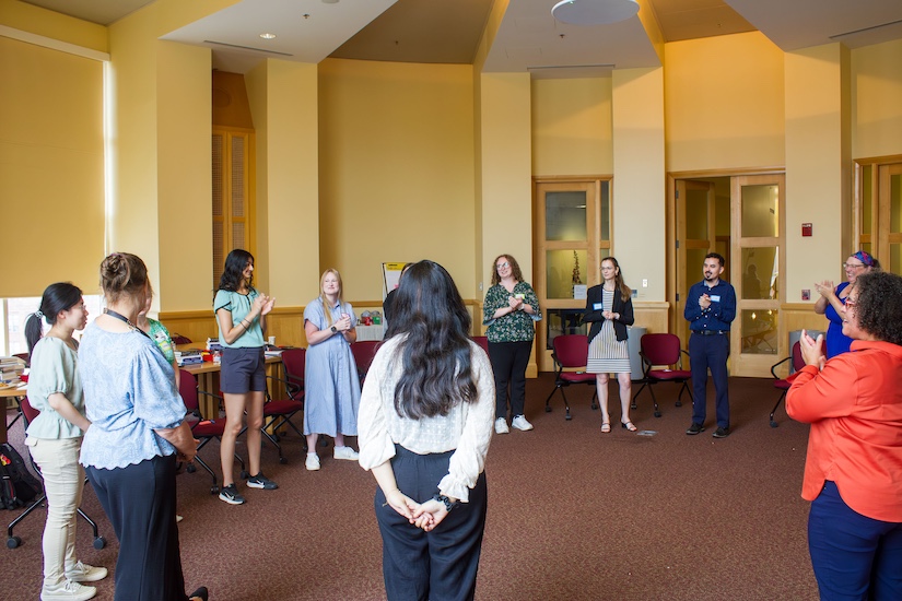 ESCAAR fellows, faculty, and improvscience facilitator are standing in a circle, facing each other, for the opening workshop of the ESCAAR Summer Institute 2026 inside the Gladhill Boardroom at UMB.